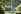 A shot of Birkbeck's campus building through trees and leaves. There is a girl sitting on the grass in front of the building. 